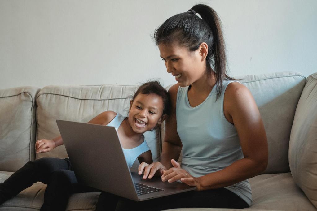ethnic mother and daughter with computer sitting on couch