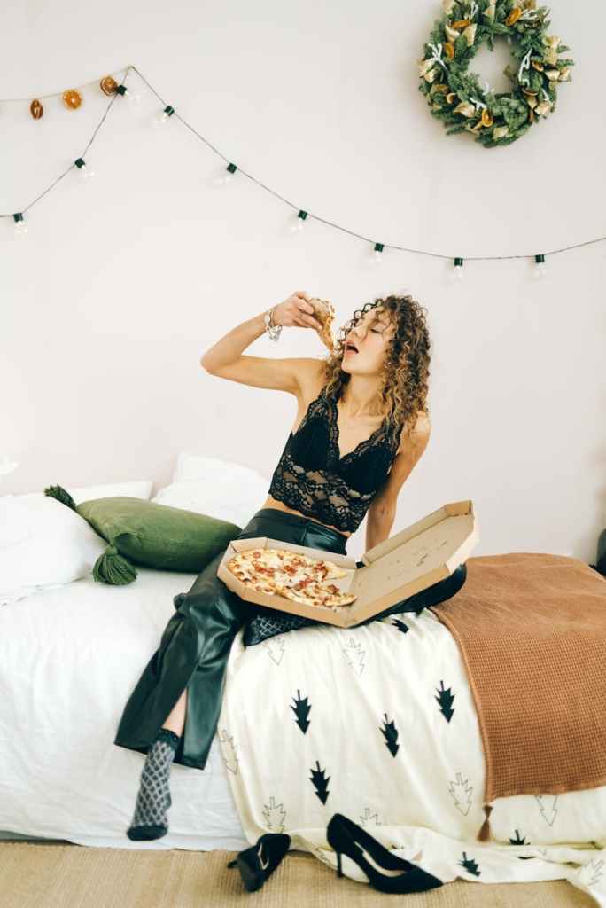 woman in black lace crop top sitting on bed eating pizza