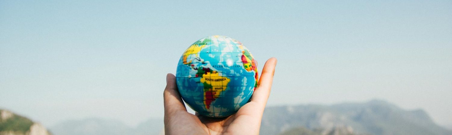 person holding world globe facing mountain