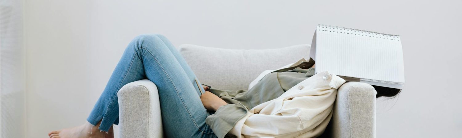 person lying on sofa chair face covered with notebook